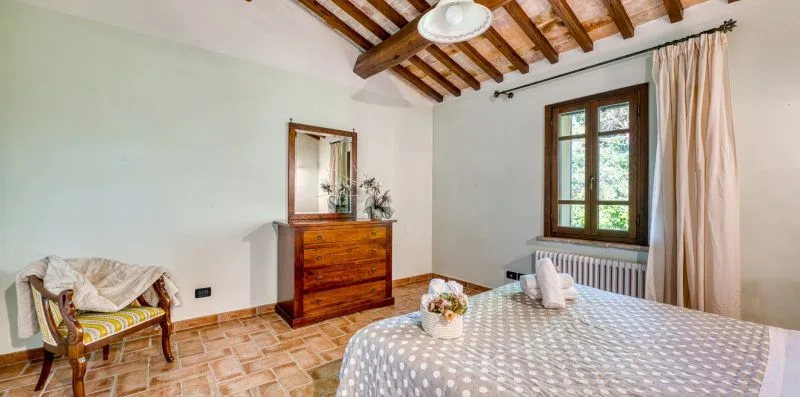 A bedroom with a patterned bedspread, wooden dresser, and window.