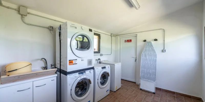 A laundry room with stacked washing machines, a sink, and an ironing board.