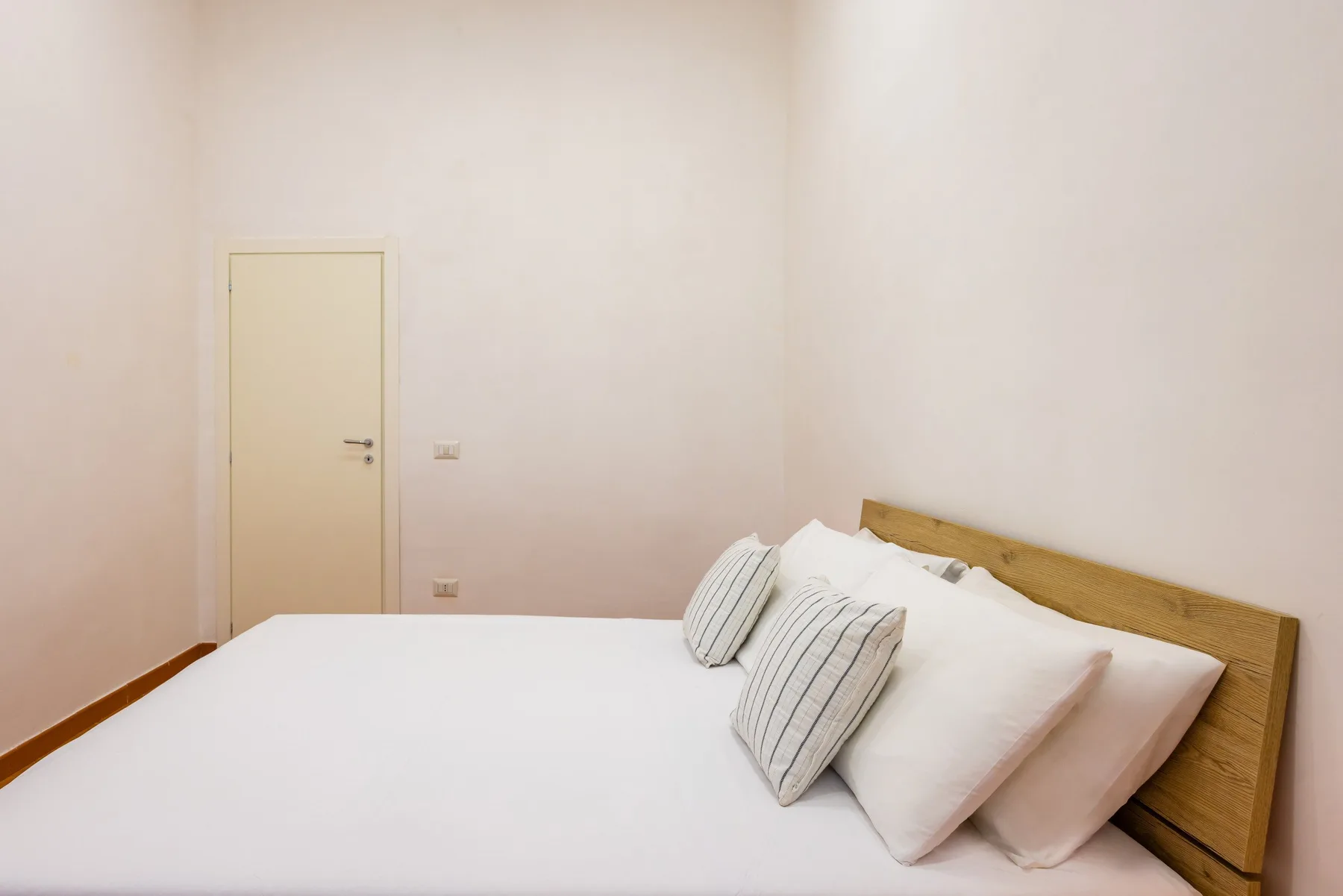 A bedroom with a bed dressed in white bedding and striped pillows.
