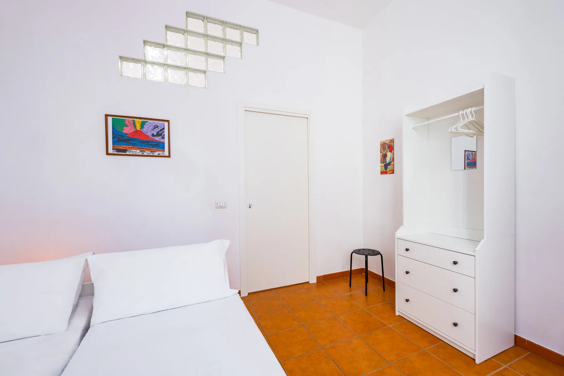 A bright bedroom with a bed, tiled floor, and open wardrobe area.