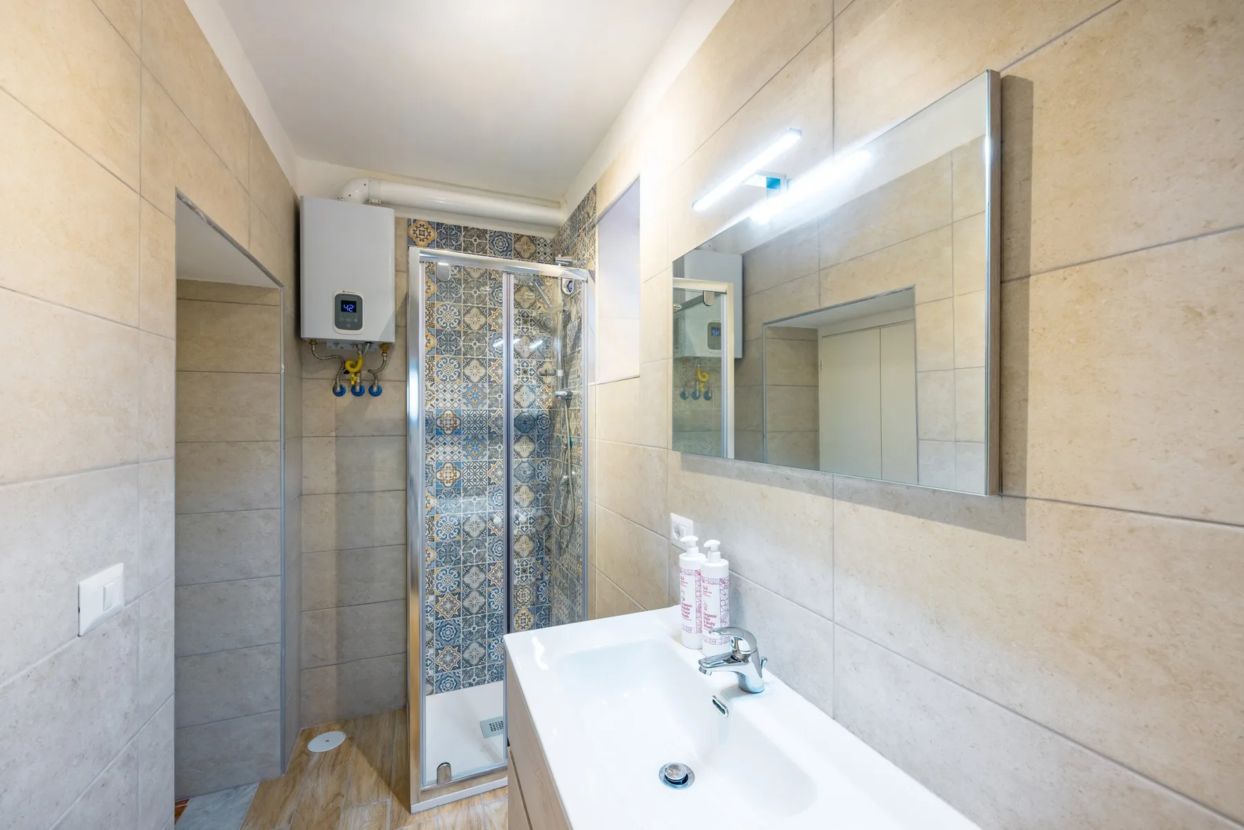 A tiled bathroom with a sink, mirror, and patterned shower screen.