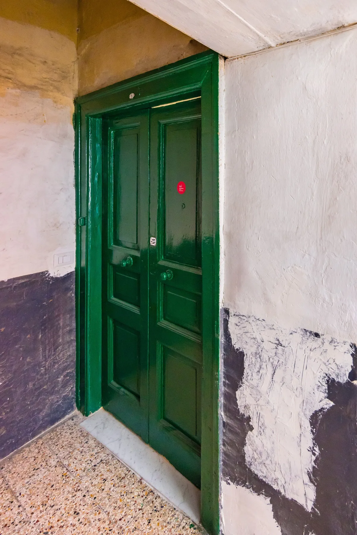 A dark green paneled door stands in a worn, two-tone hallway.