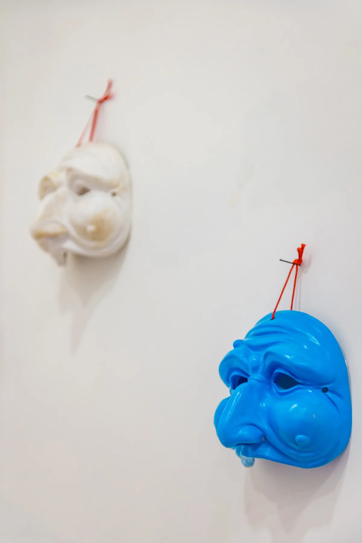 Two sculpted face masks hang on a plain wall, one white and one blue.