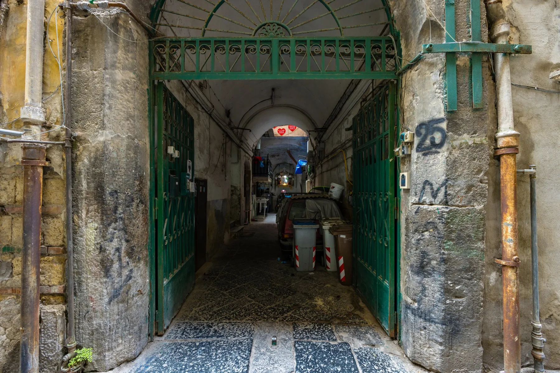 A narrow stone passageway leads through an open green metal gate.