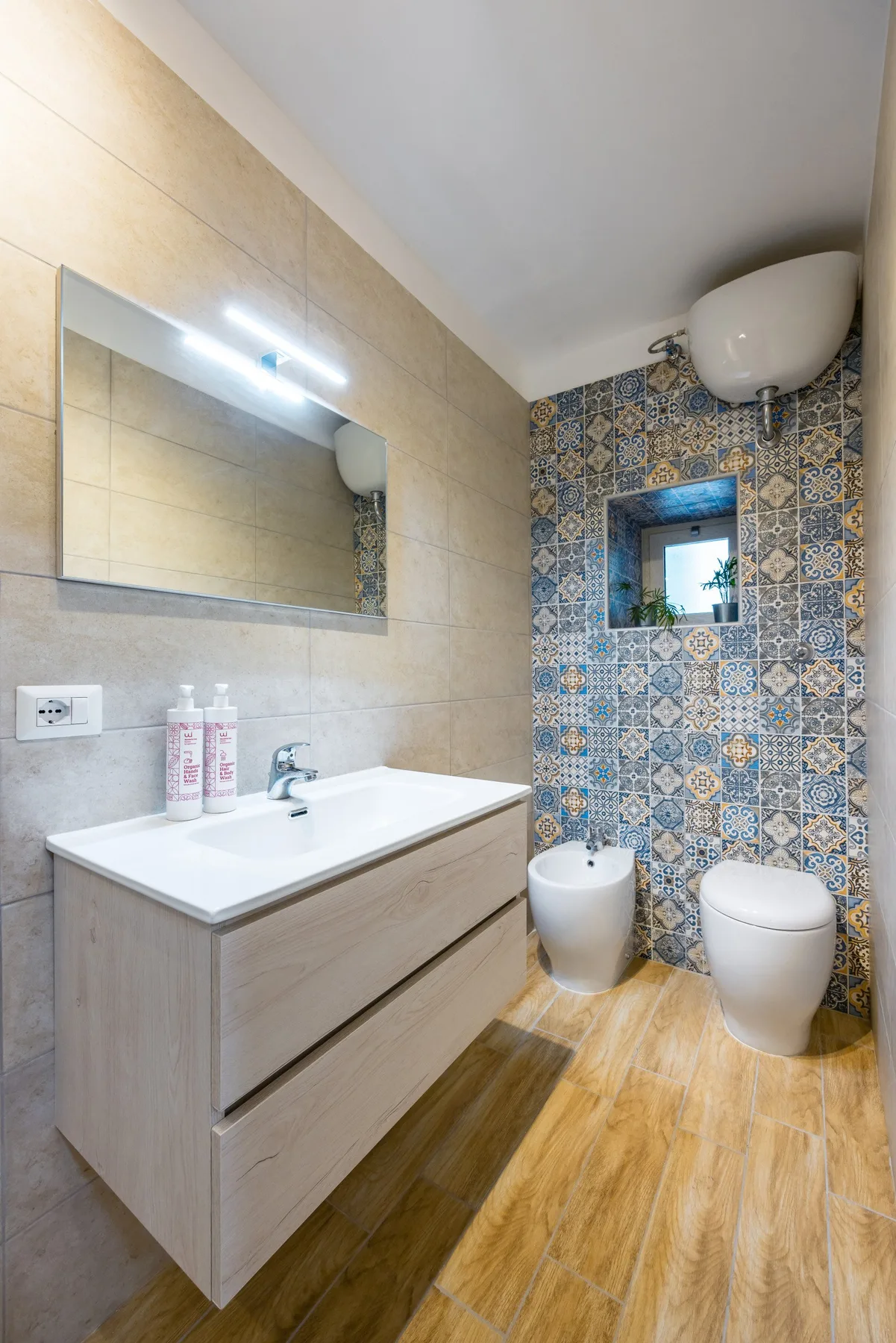 A tiled bathroom with a long vanity, patterned wall tiles, and white fixtures.