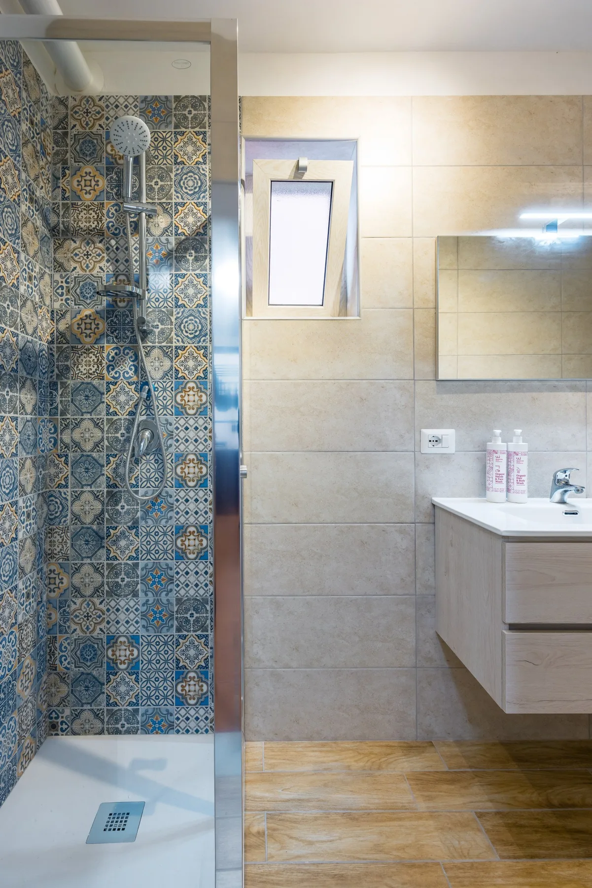 A tiled bathroom with a shower, sink, and wall mirror.
