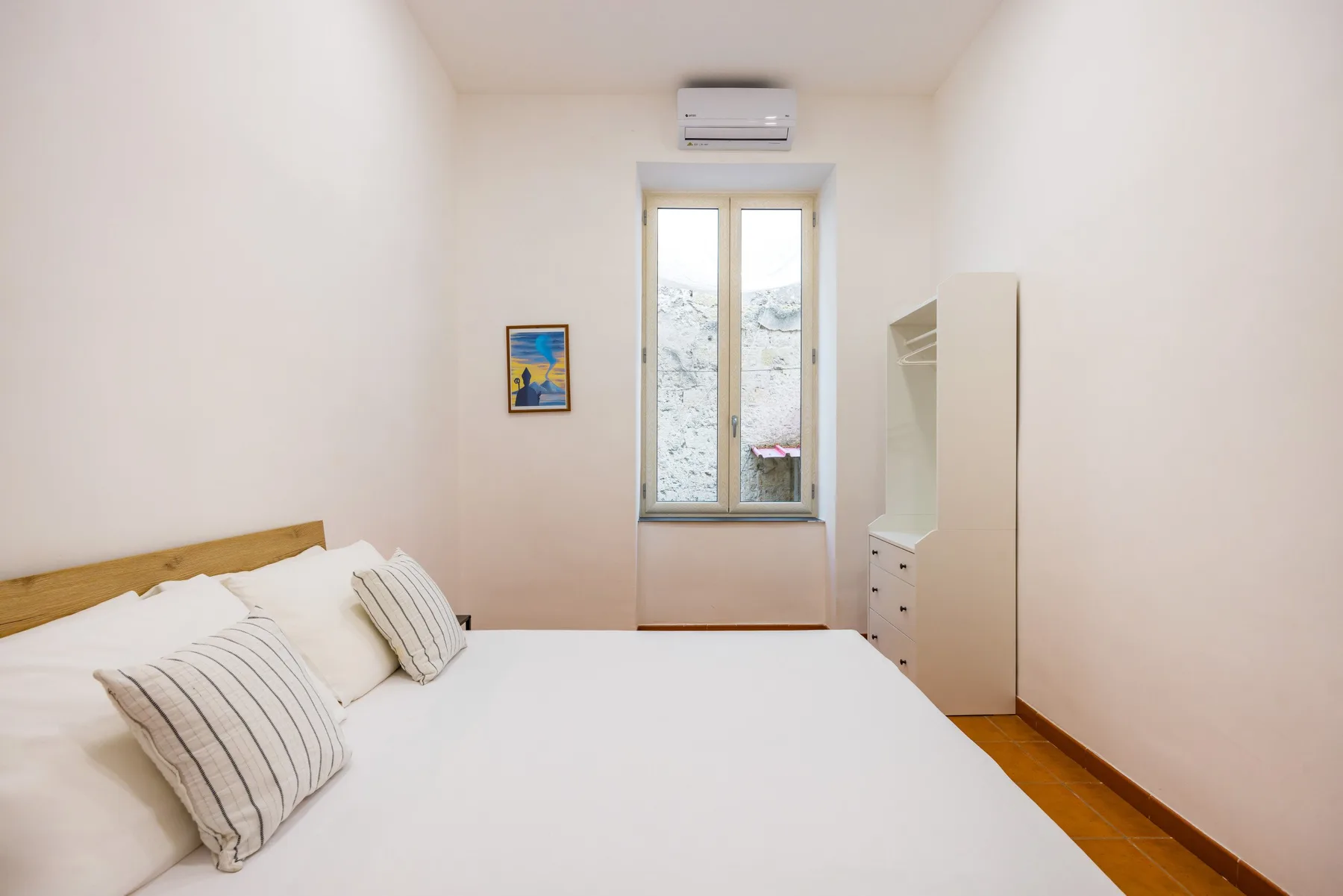 A bright bedroom with a bed, window, and wall-mounted air conditioner.