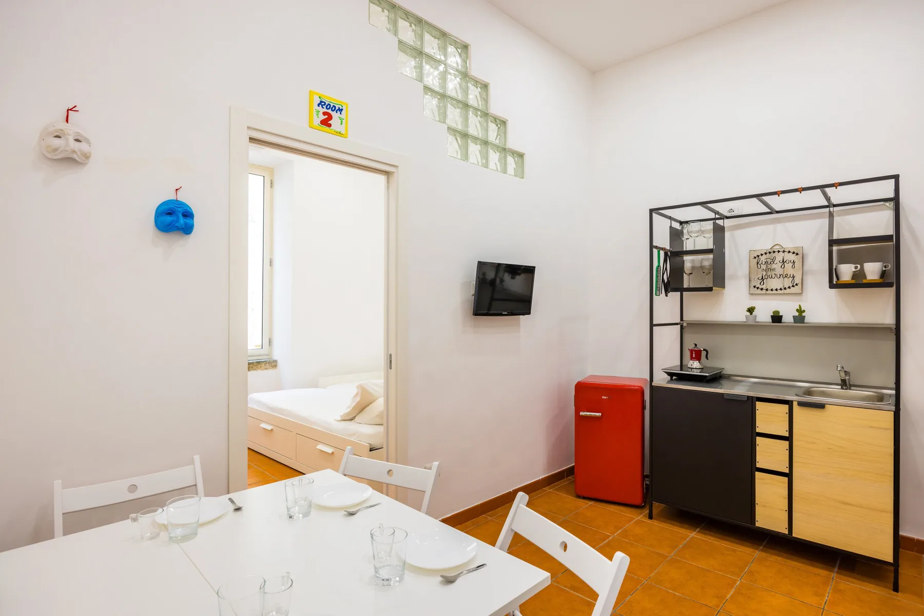 A bright dining and kitchenette area with a table, shelving, and a compact refrigerator.