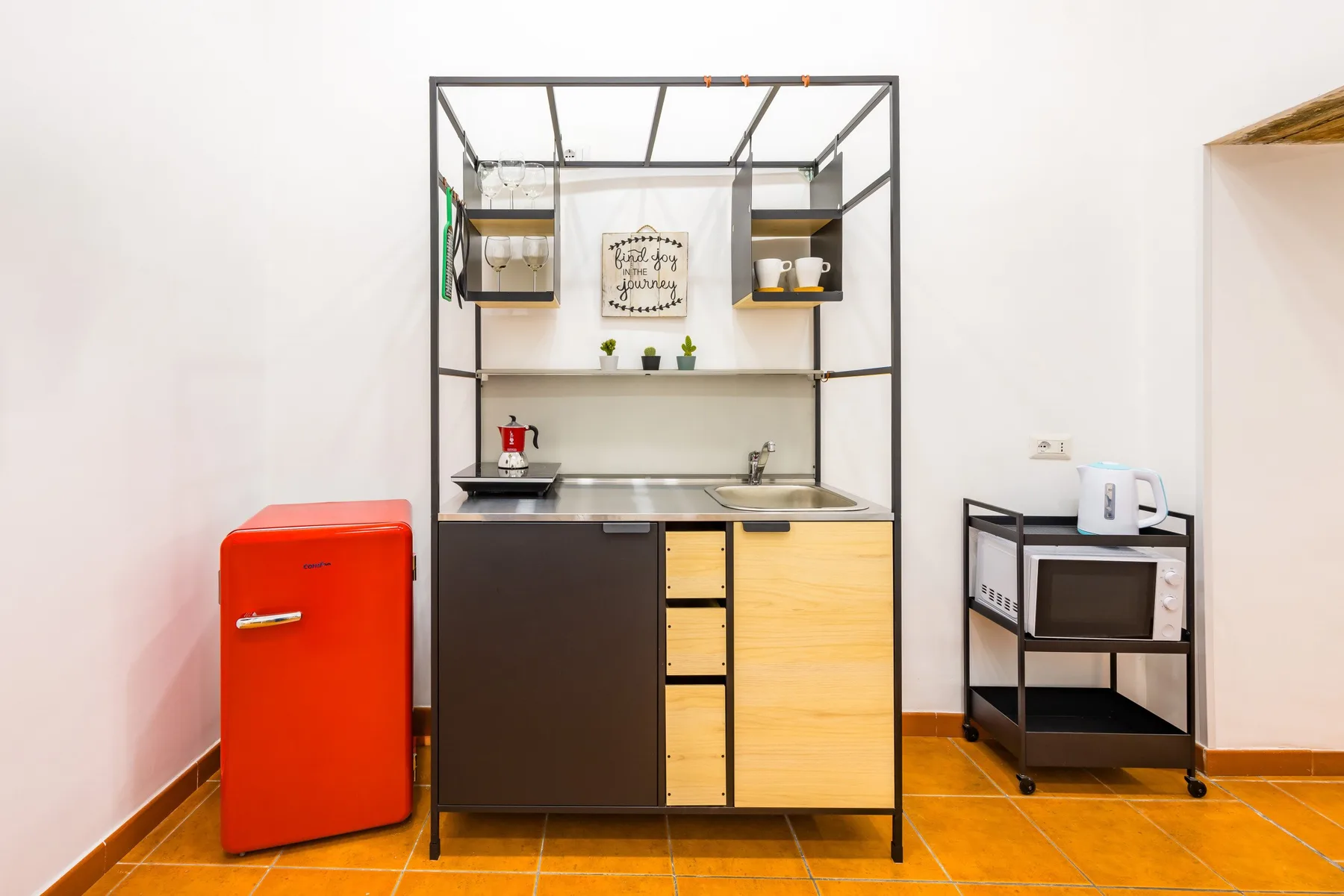 A compact kitchen area with a red refrigerator beside a counter and open shelving.