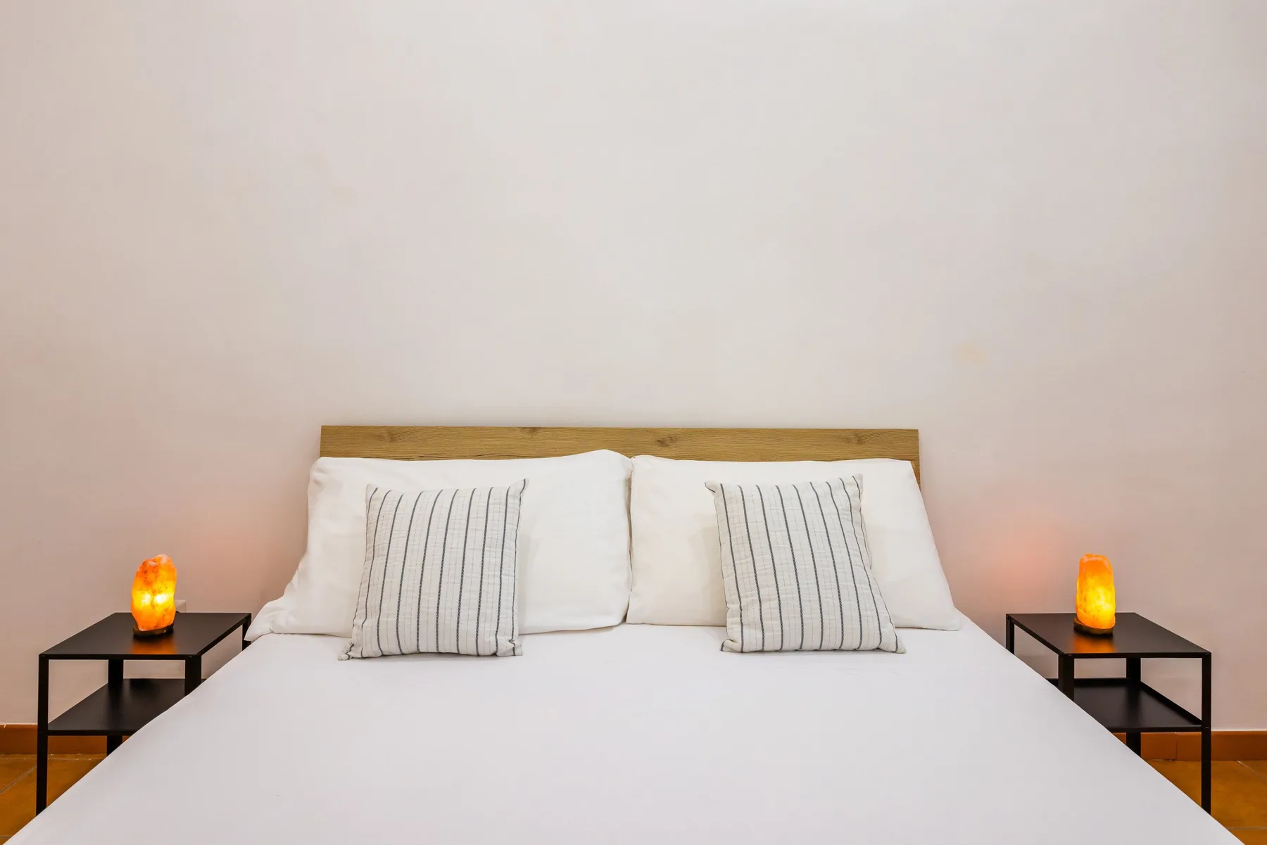 A bedroom with a neatly made bed, striped pillows, and bedside tables.