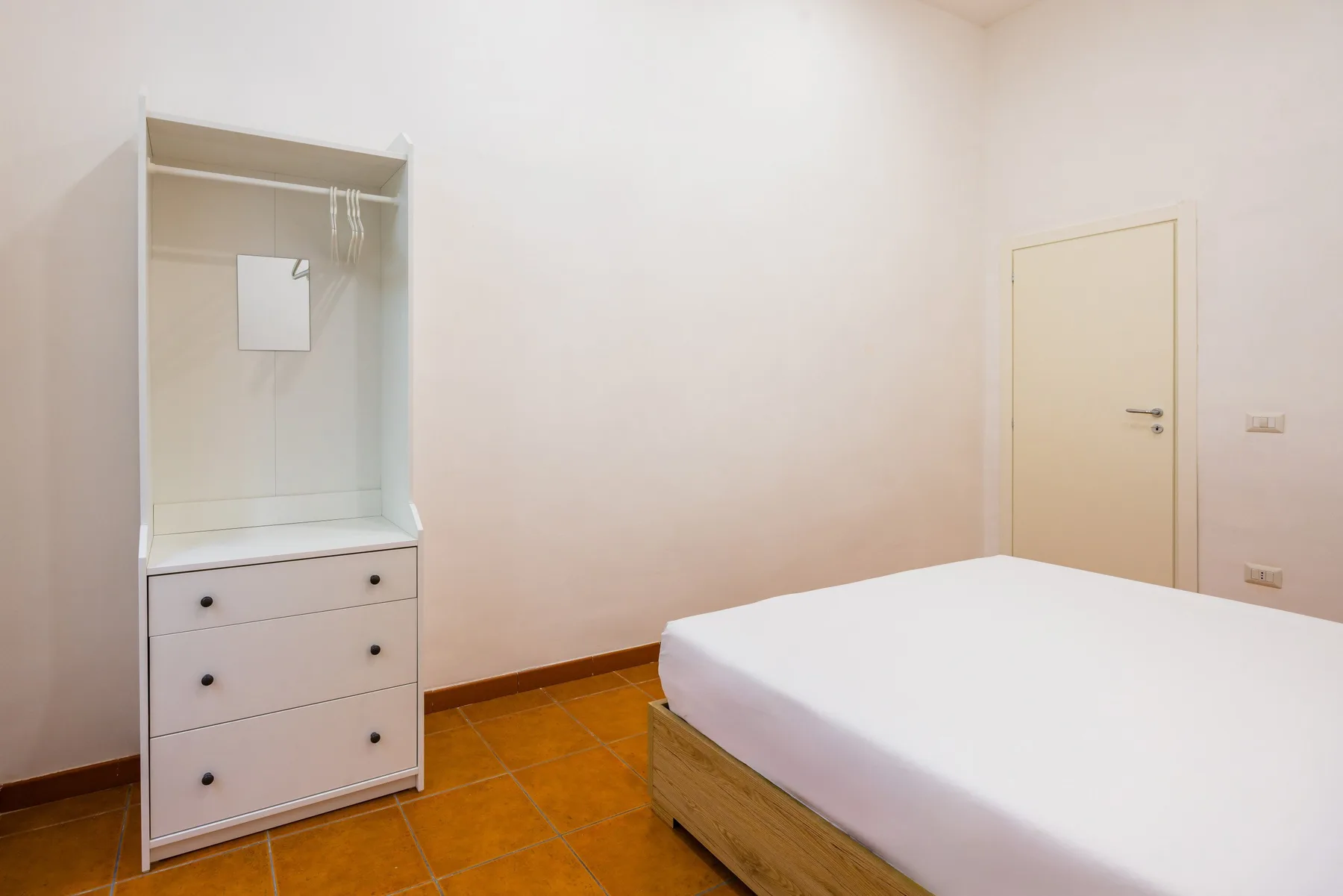 A simple bedroom with a white bed and a dresser with a mirror.