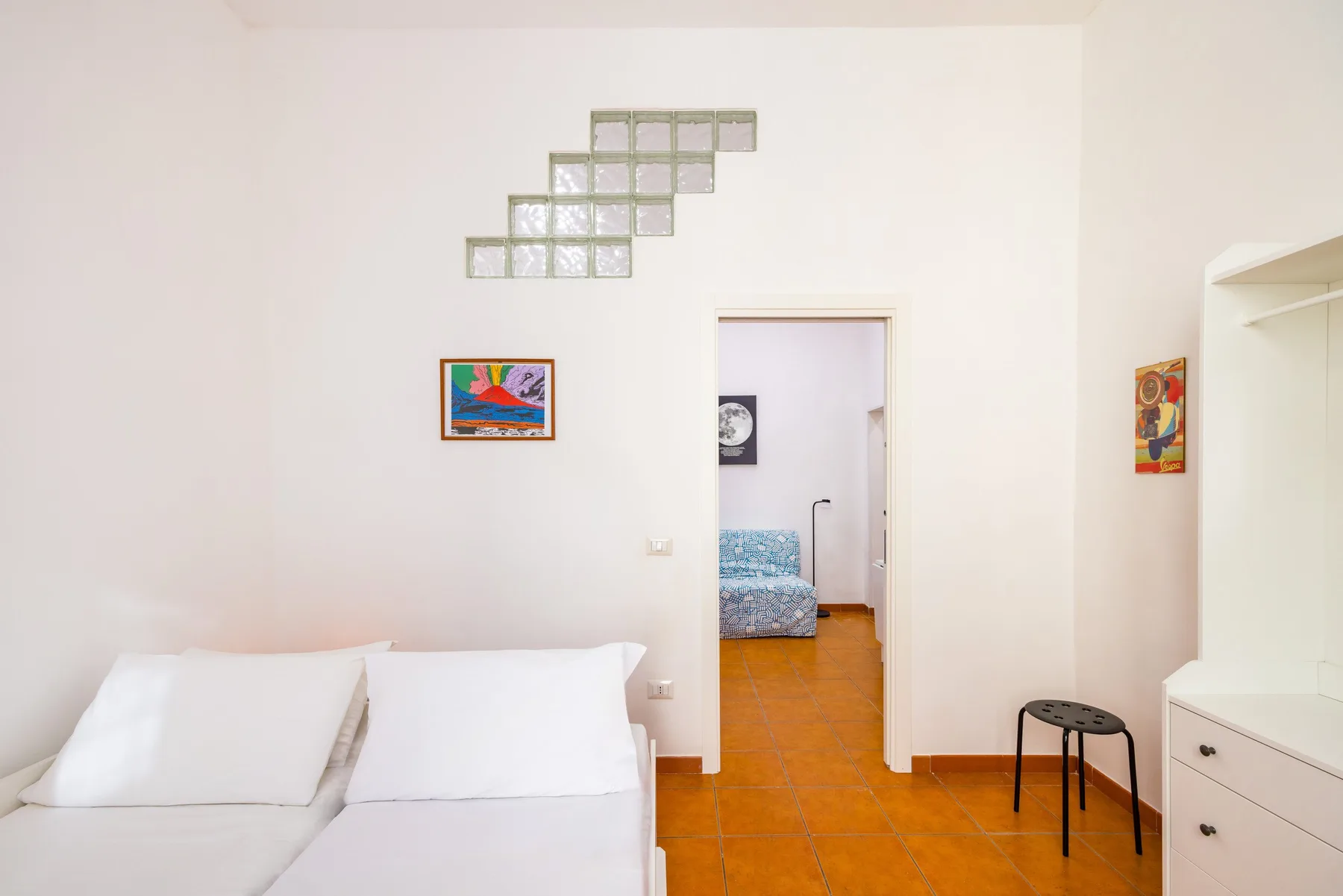 A bright bedroom with a bed, framed artwork, and a doorway to another room.