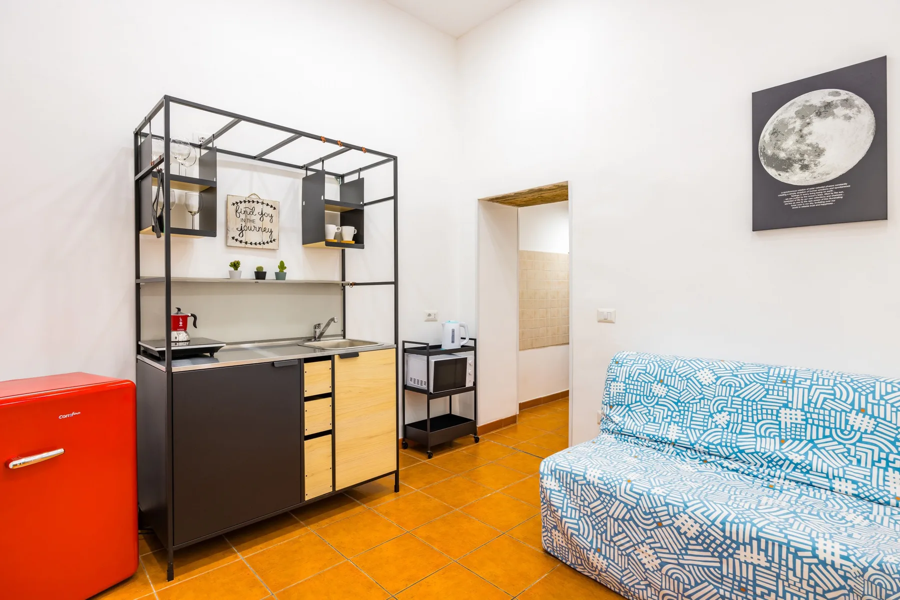 A compact kitchen and seating area with a patterned couch and red refrigerator.