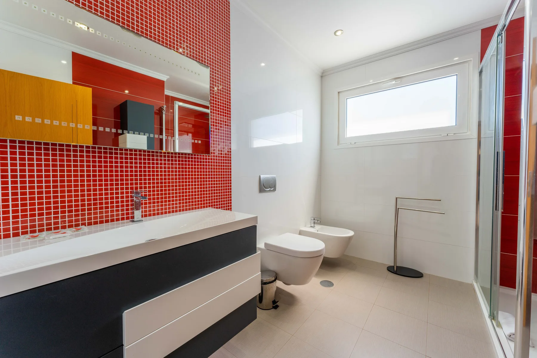 Un baño luminoso con un mueble de lavabo amplio, azulejos rojos y una ducha de vidrio.