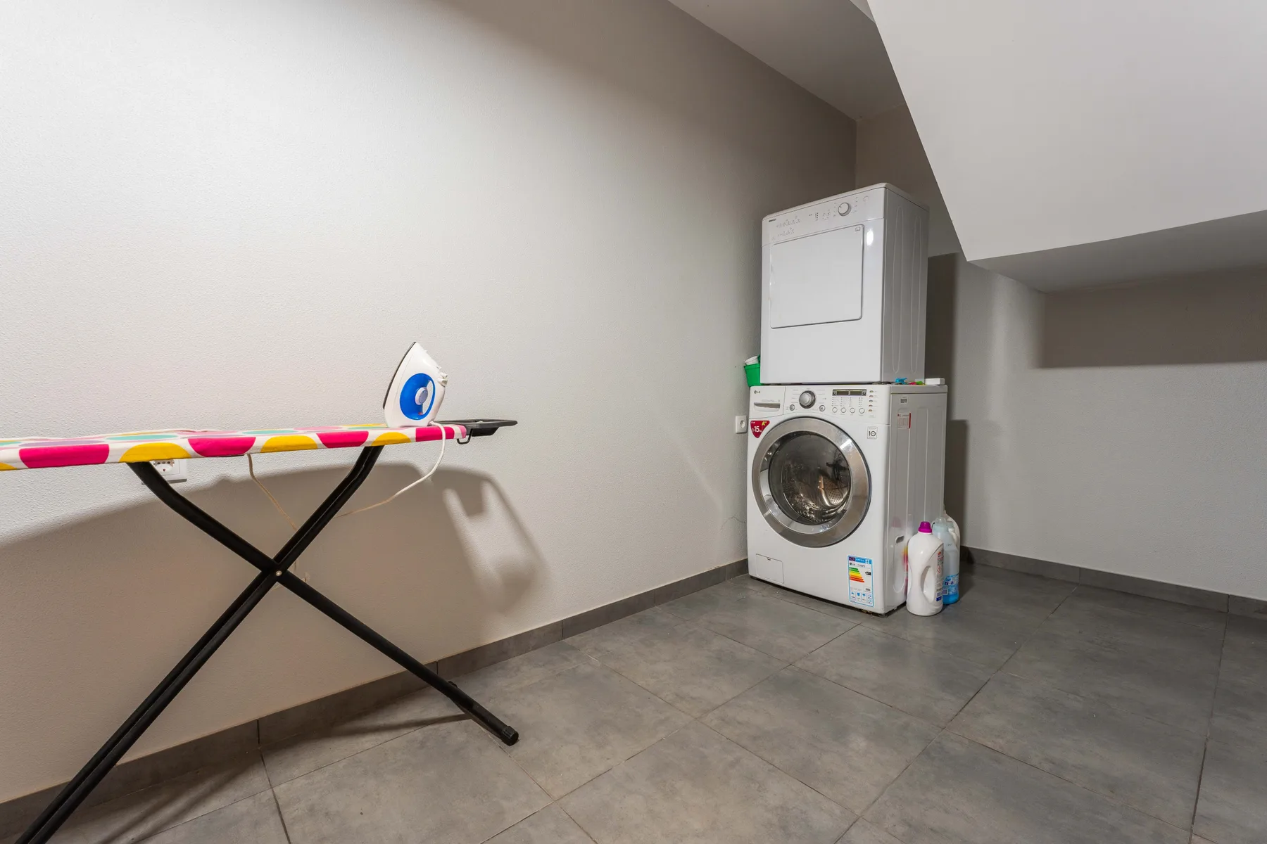 Un cuarto de lavandería con lavadora, secadora y tabla de planchar.