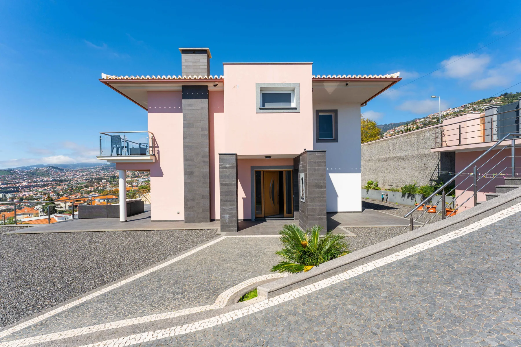 Exterior de una casa rosa moderna con entrada central y vistas a la ladera.