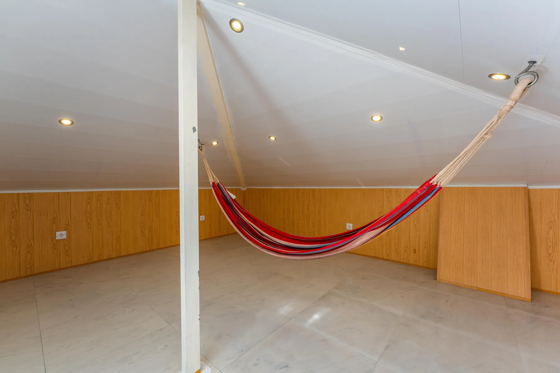 Una luminosa habitación abuhardillada con una hamaca a rayas sobre el suelo de baldosas.