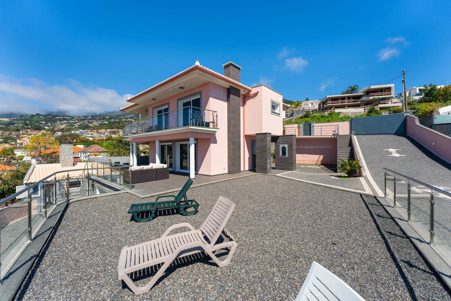 Una casa rosa da a una terraza pavimentada con asientos reclinables y vistas a las colinas.