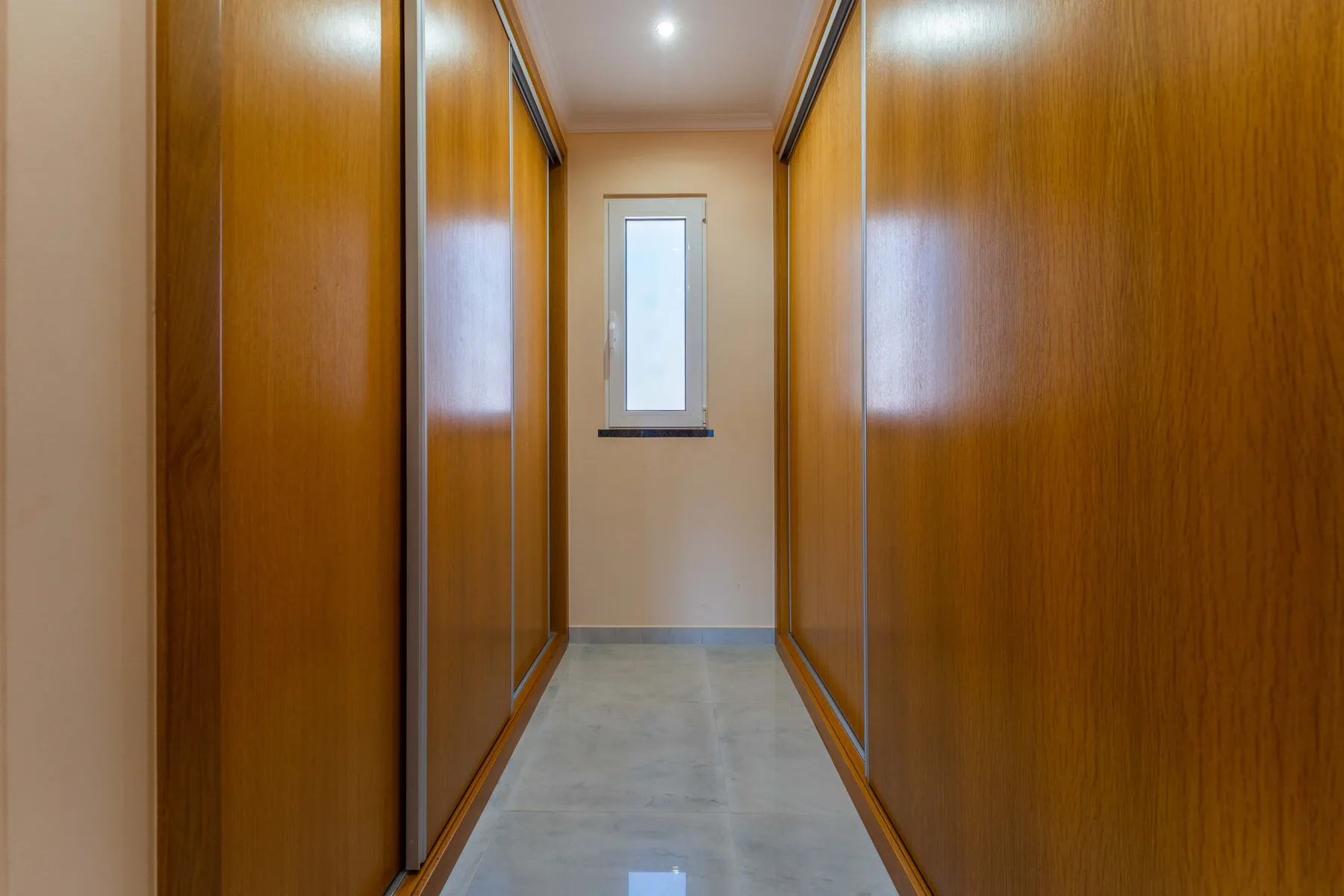 Pasillo con puertas de armario de madera y una ventana pequeña al fondo.