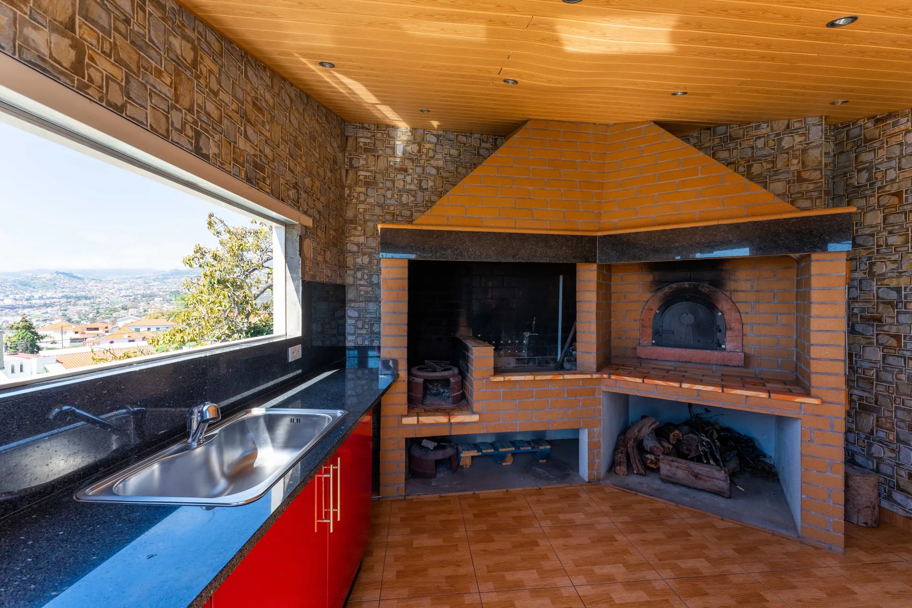 Zona de barbacoa de ladrillo con fregadero y encimera bajo un techo de madera.