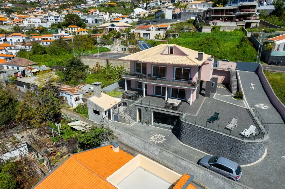 Una casa en una ladera con terraza pavimentada y viviendas cercanas.