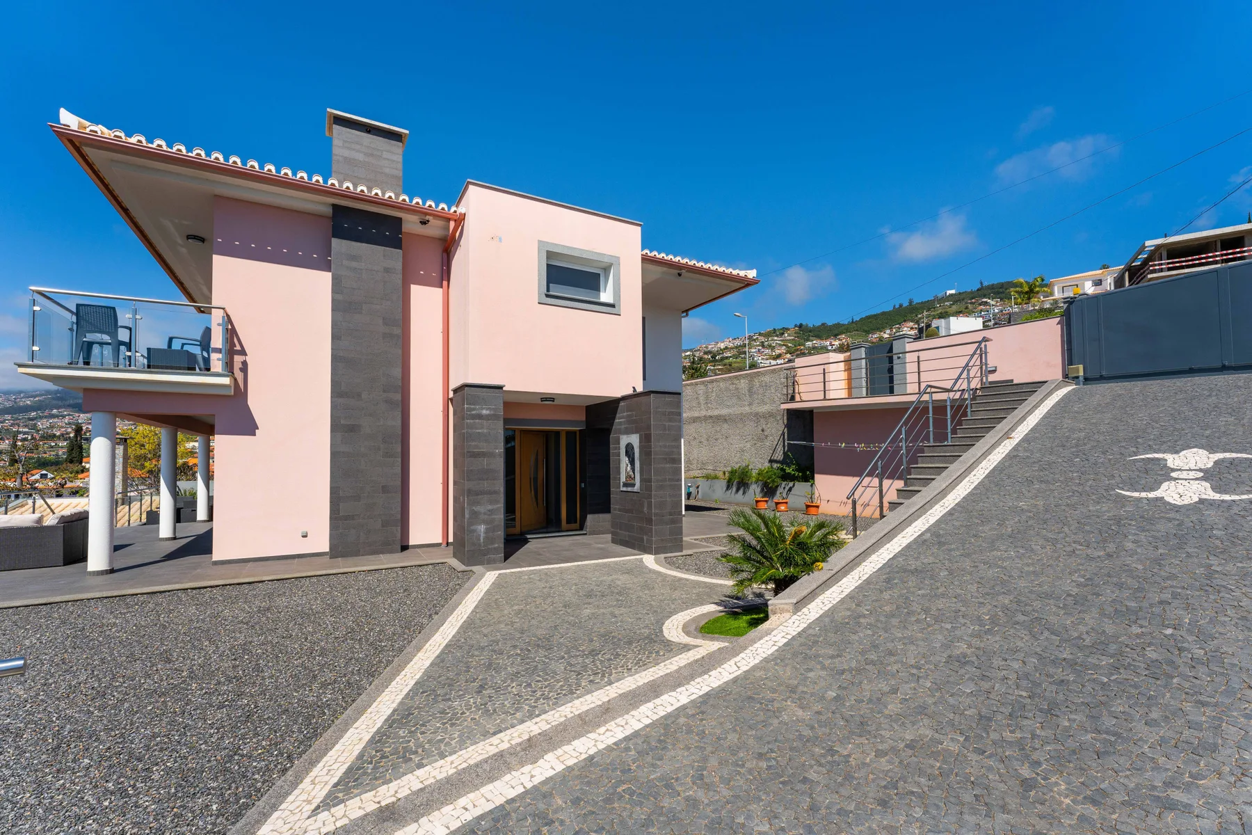 Una casa rosa moderna se encuentra junto a una entrada pavimentada bajo un cielo despejado.