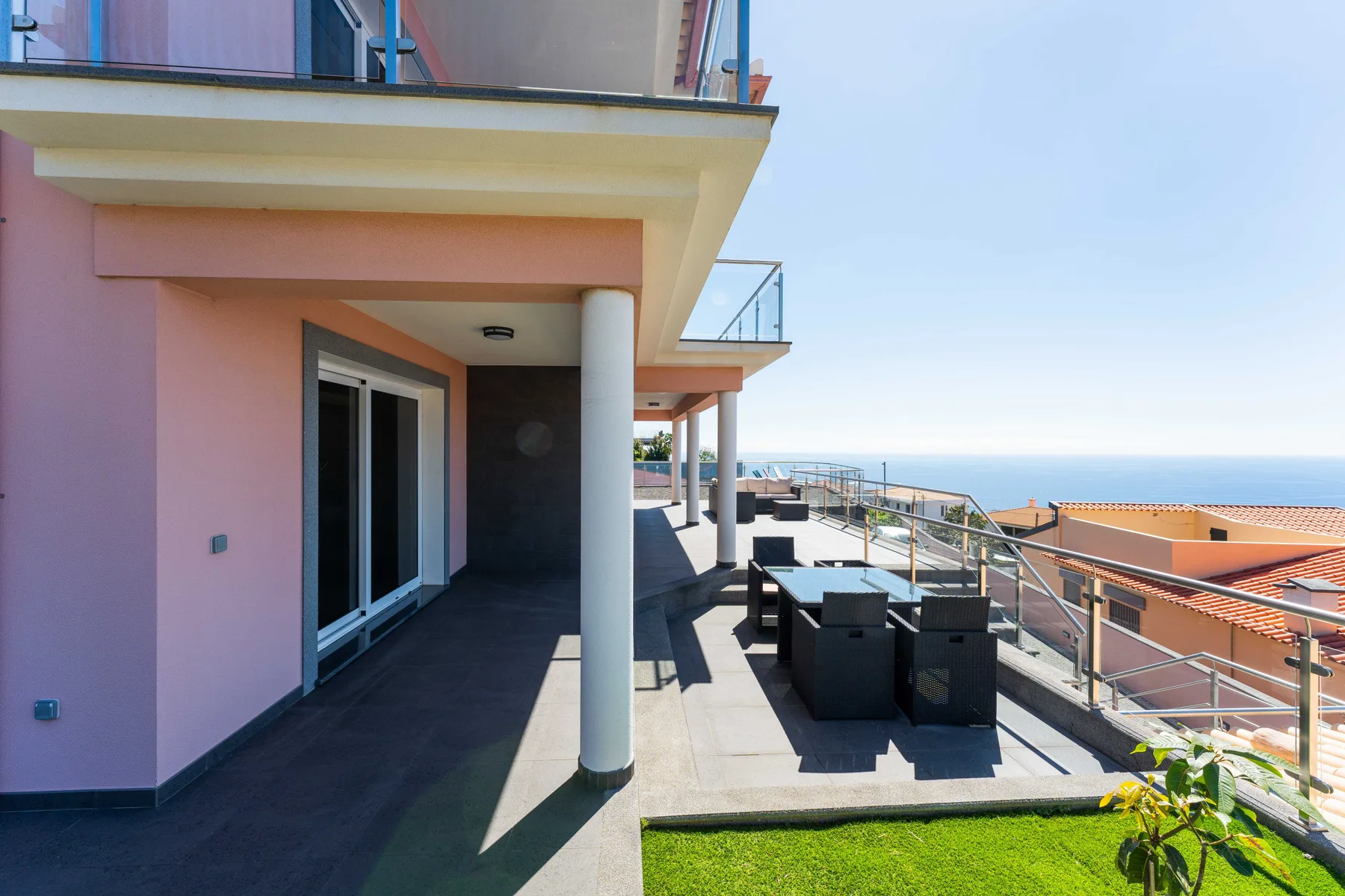Terraza exterior con asientos junto a un edificio rosa, con vistas a tejados cercanos.