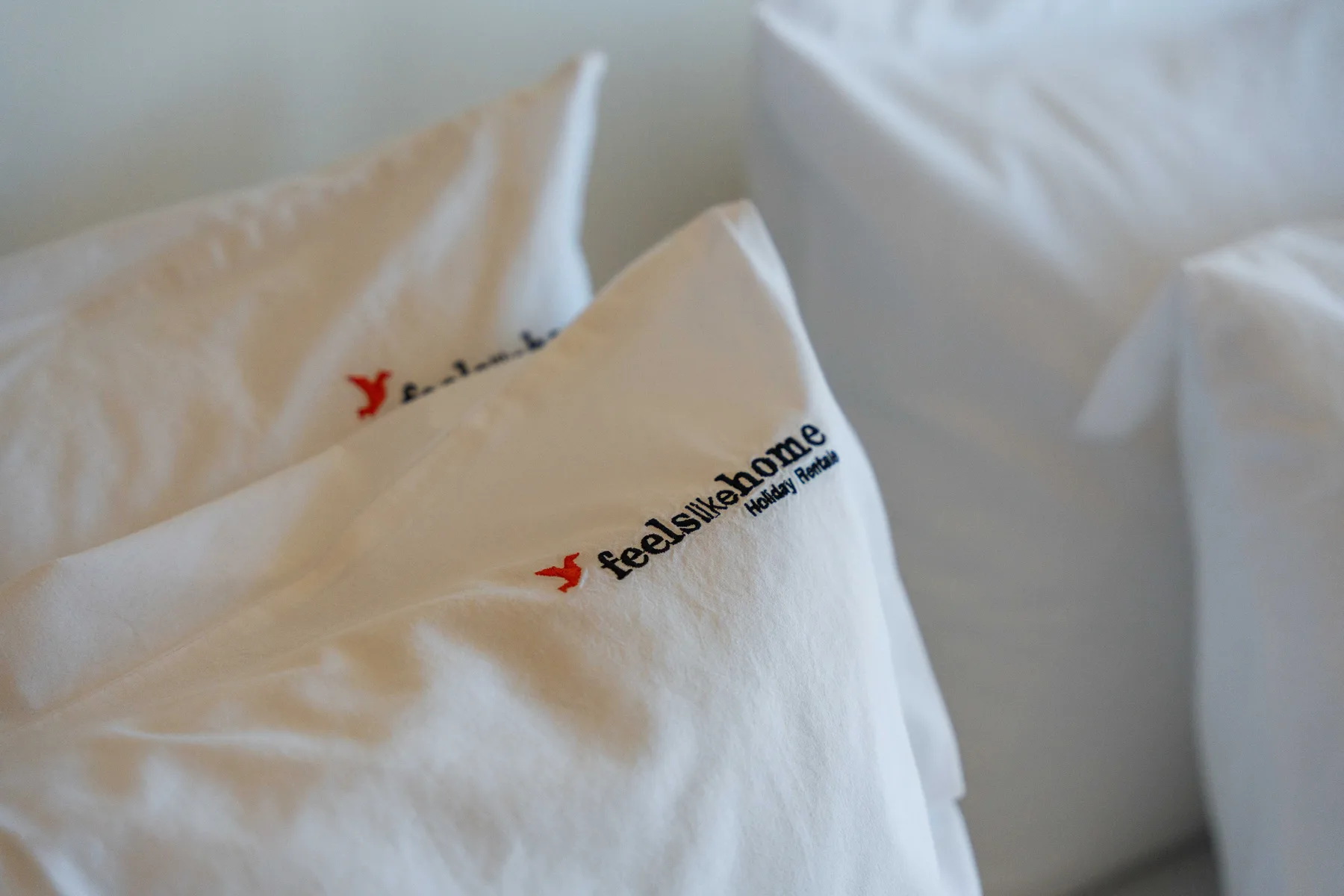 Una cama con almohadas blancas, una de ellas con un pequeño logotipo impreso.