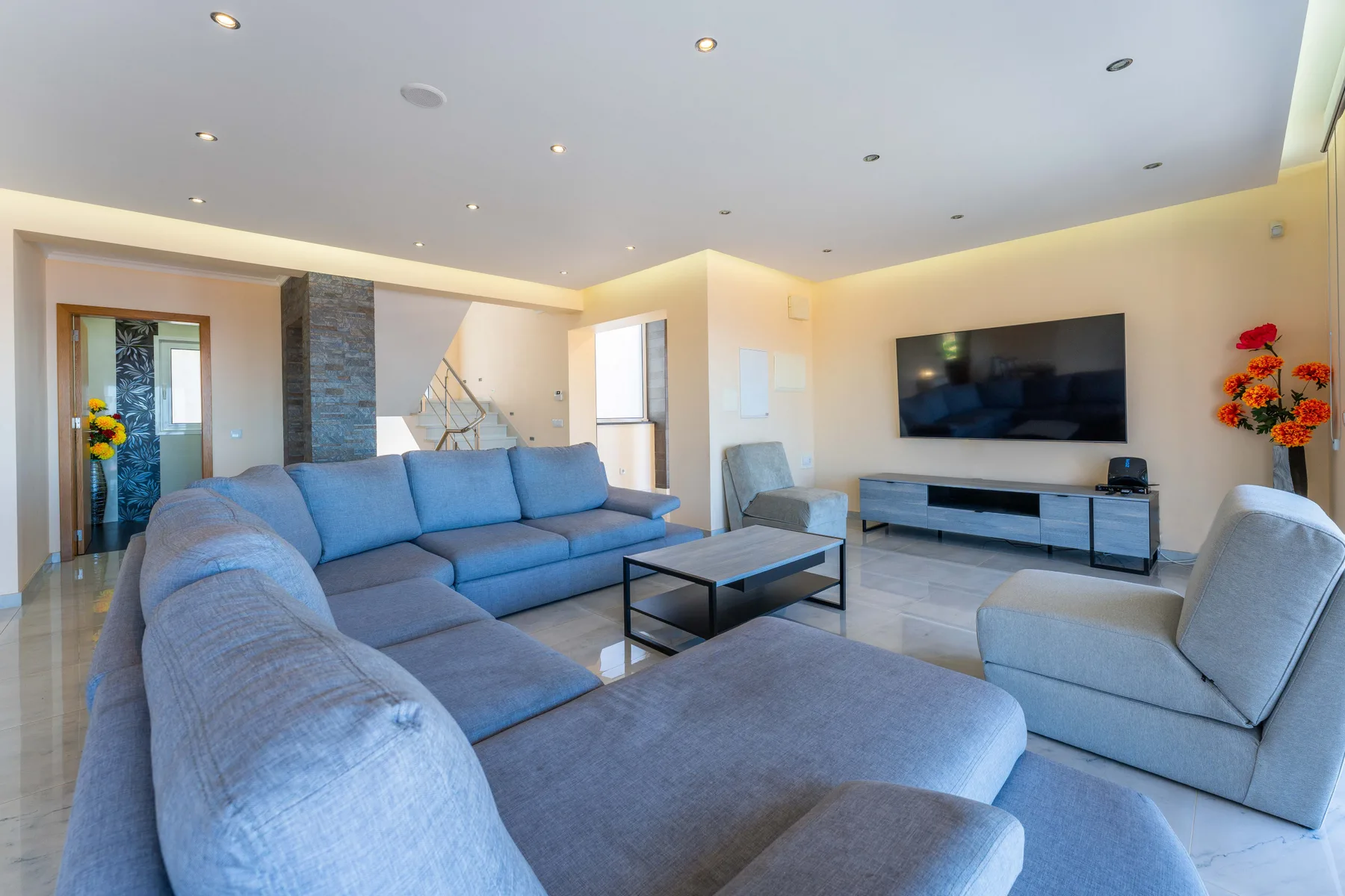 Una sala de estar luminosa con asientos azules, una mesa de centro y un televisor en la pared.