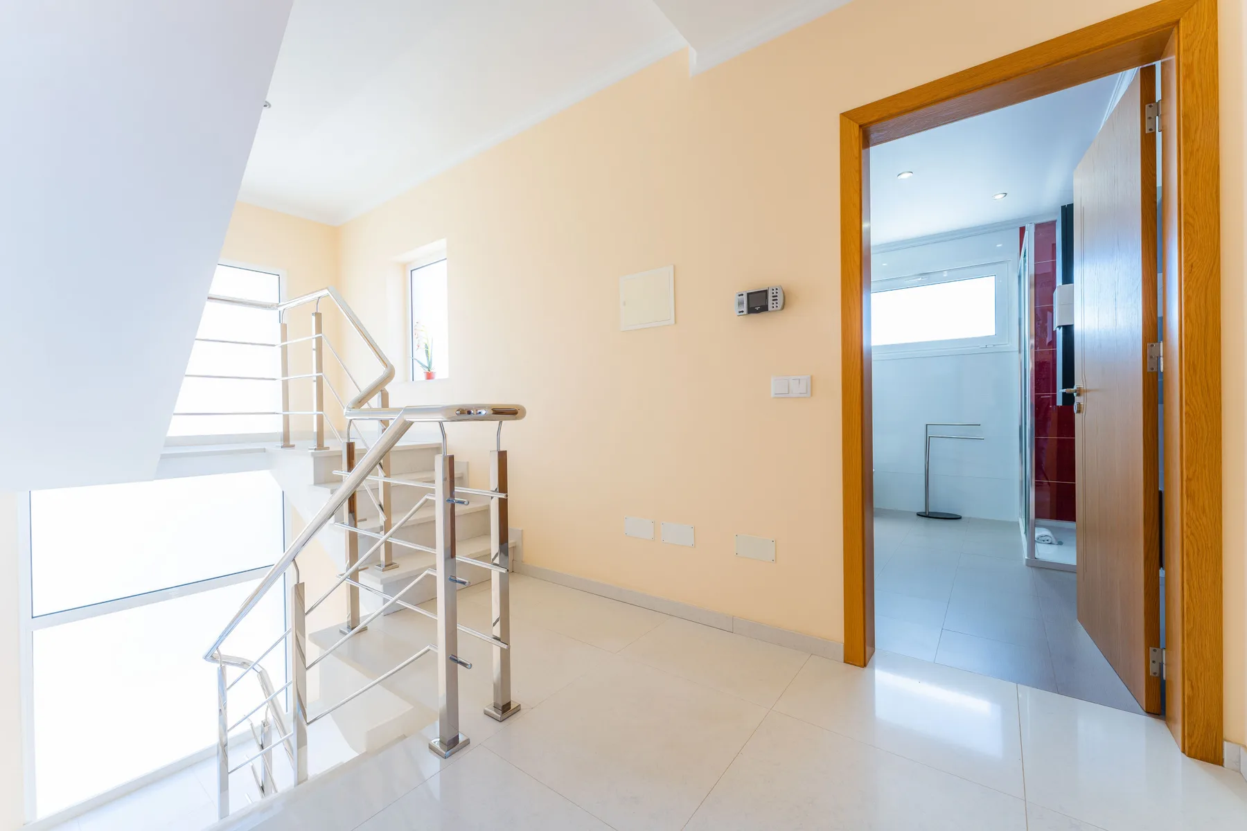 Un pasillo interior luminoso da a una escalera y un baño con suelo de baldosas.