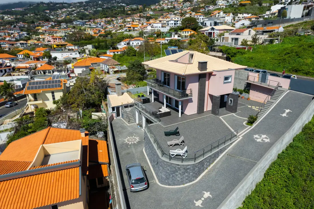 Una casa en la ladera con patio pavimentado y viviendas alrededor.