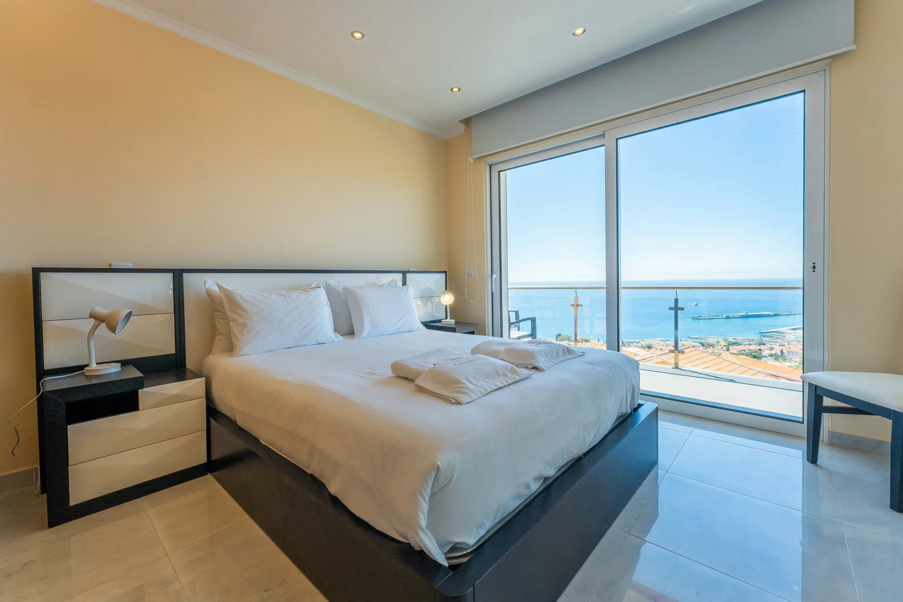 Un dormitorio con una cama junto a grandes ventanales con vistas al mar.
