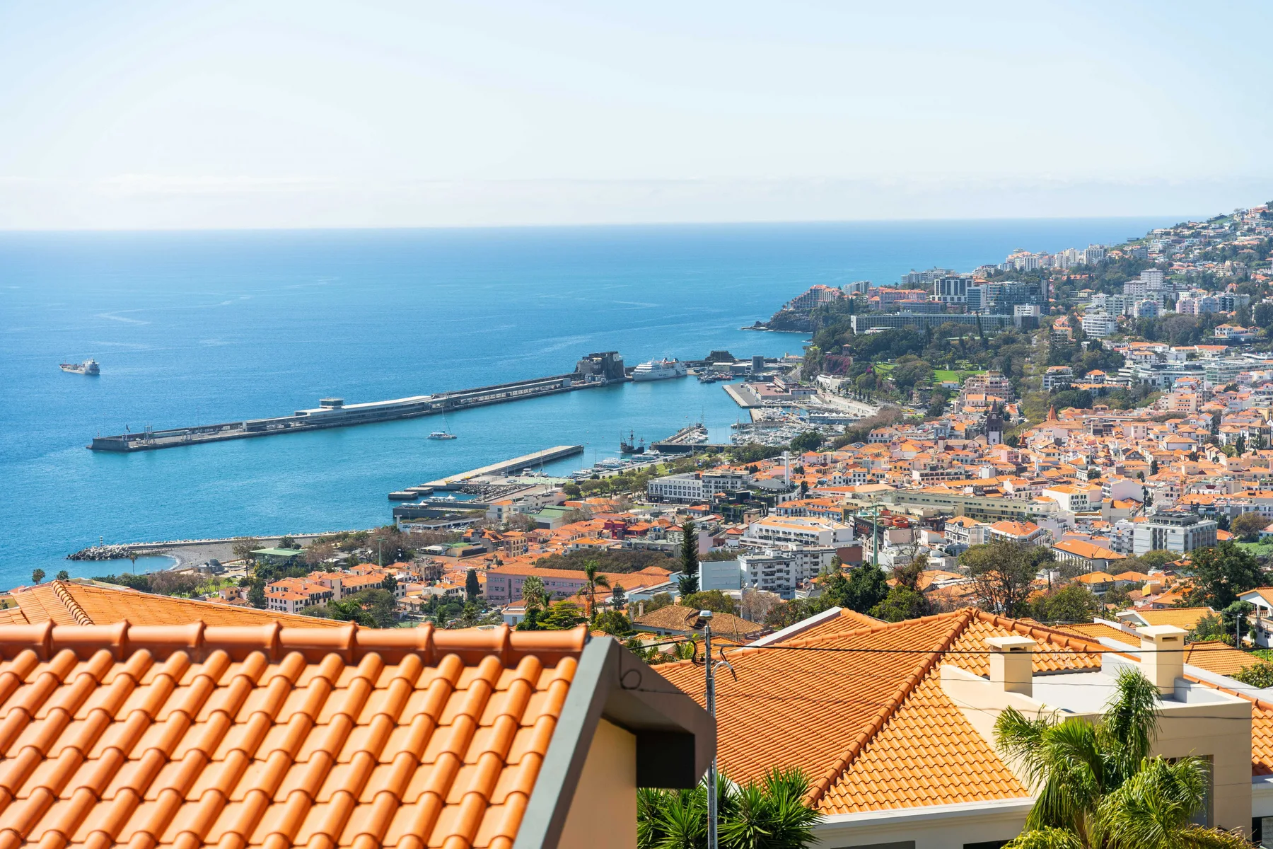 Paisaje costero urbano con un puerto y el mar más allá de tejados de tejas.