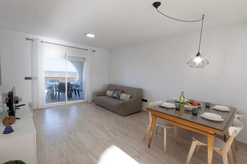 Una luminosa sala de estar y comedor con un sofá y una mesa junto a puertas corredizas de vidrio.