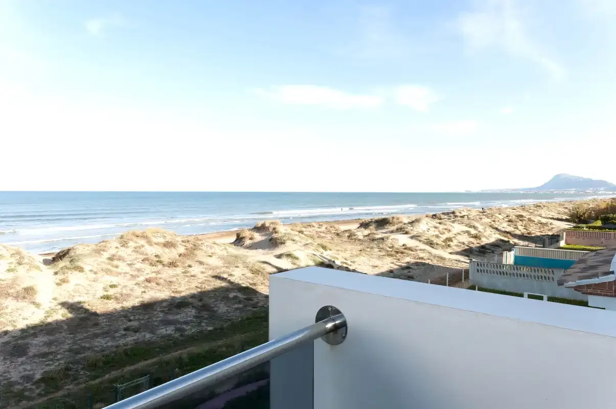 A balcony overlooks sandy dunes and the ocean under a bright sky.