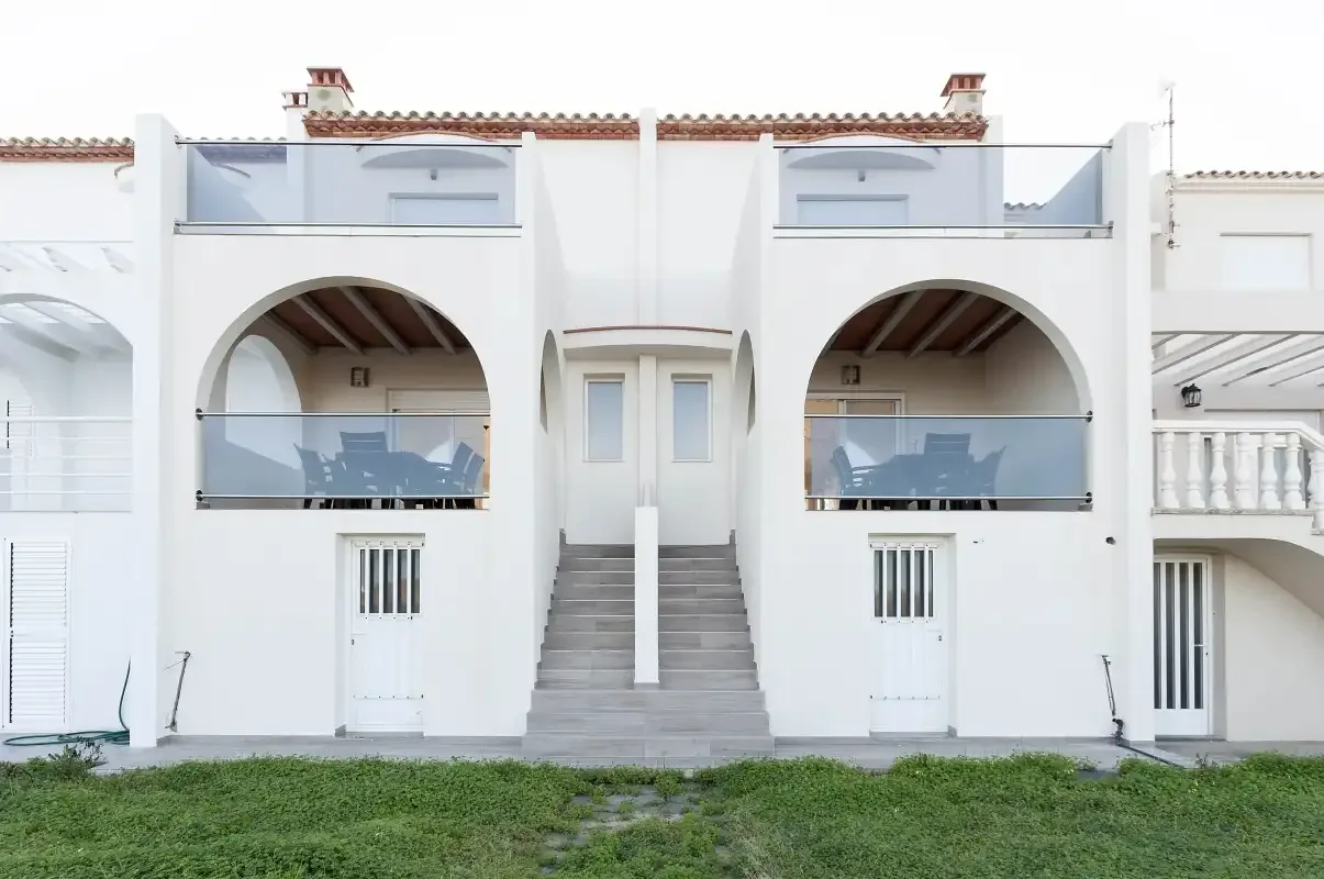White residential building facade with arched balconies and a central staircase.