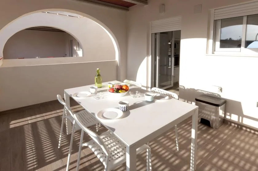 Un comedor luminoso con una mesa blanca y sillas junto a grandes ventanas.