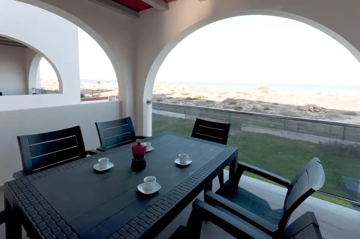 A covered terrace has a dining table and seating overlooking the beach.