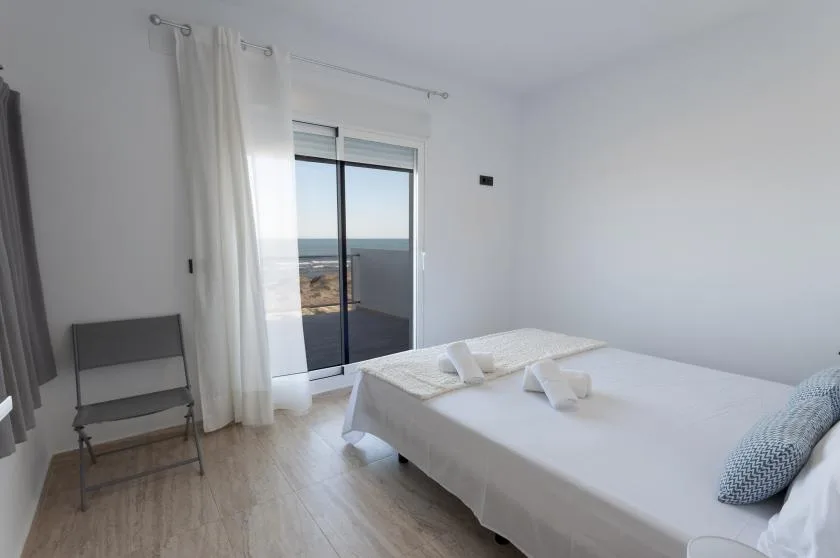 A bright bedroom with a bed beside sliding glass doors and curtains.