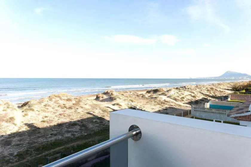 A balcony railing overlooks sandy dunes and the ocean.