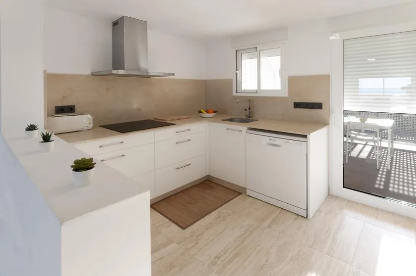 A bright kitchen with white cabinets, a cooktop, and a window above the counter.