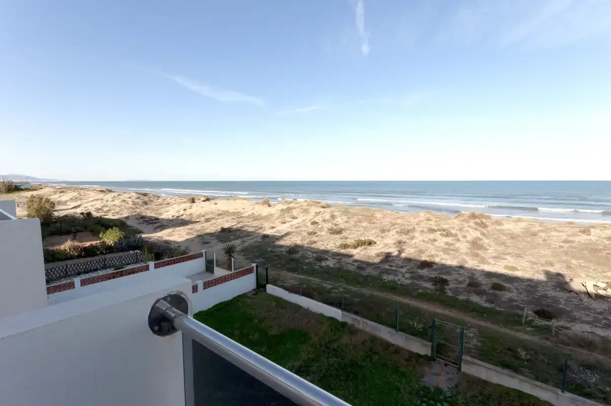 A coastal view shows sandy dunes and the sea beyond a balcony railing.