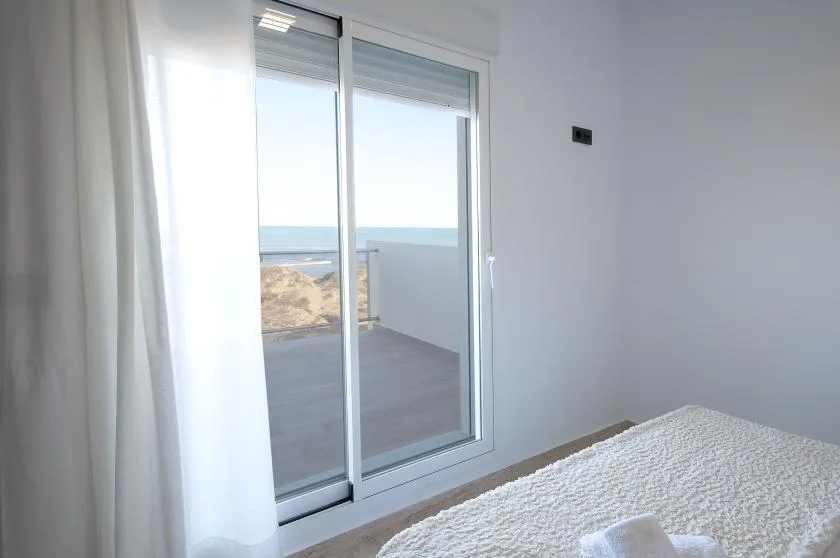 A bedroom with a bed beside sliding glass doors opening onto a balcony with a sea view.