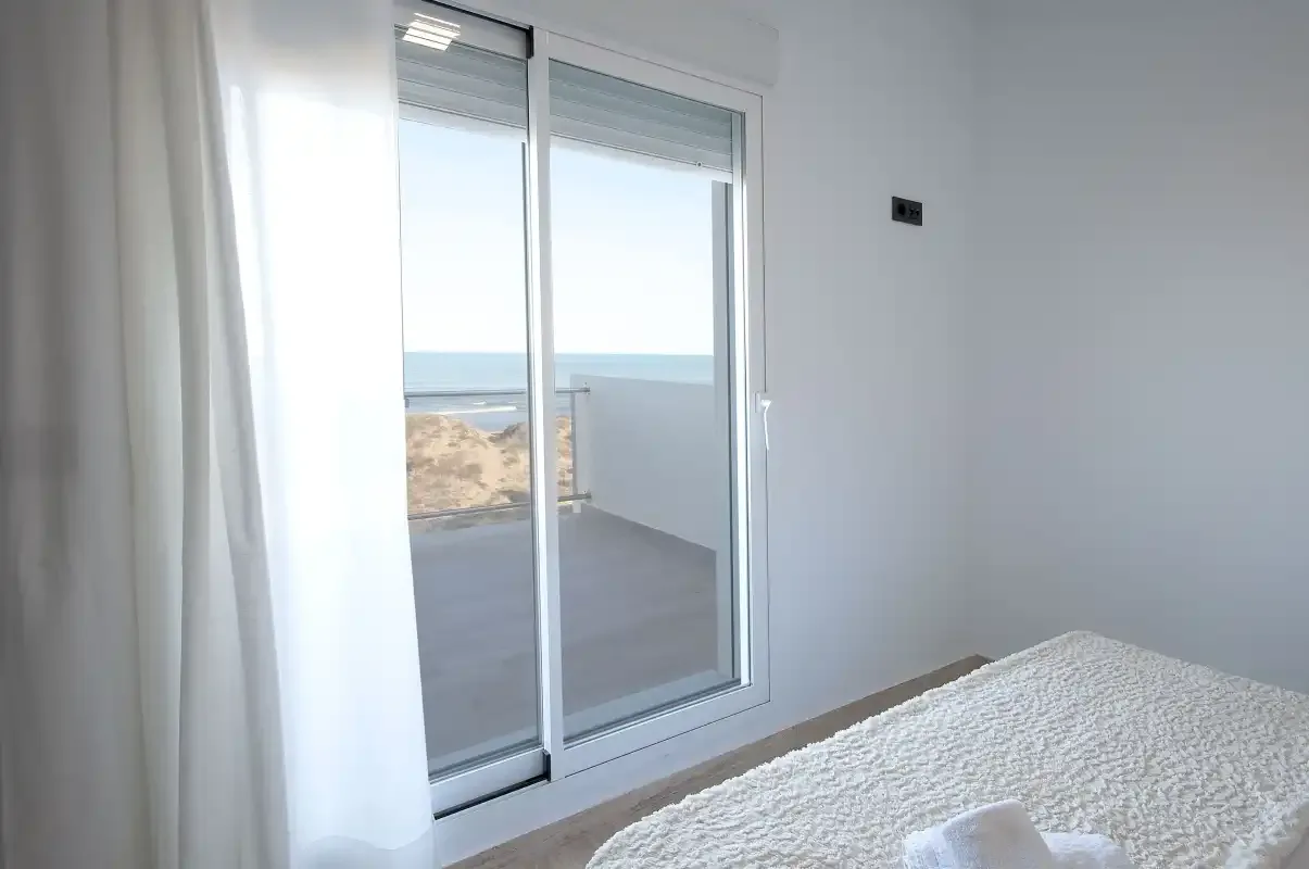 A bright bedroom opens onto a balcony with a view of the sea.