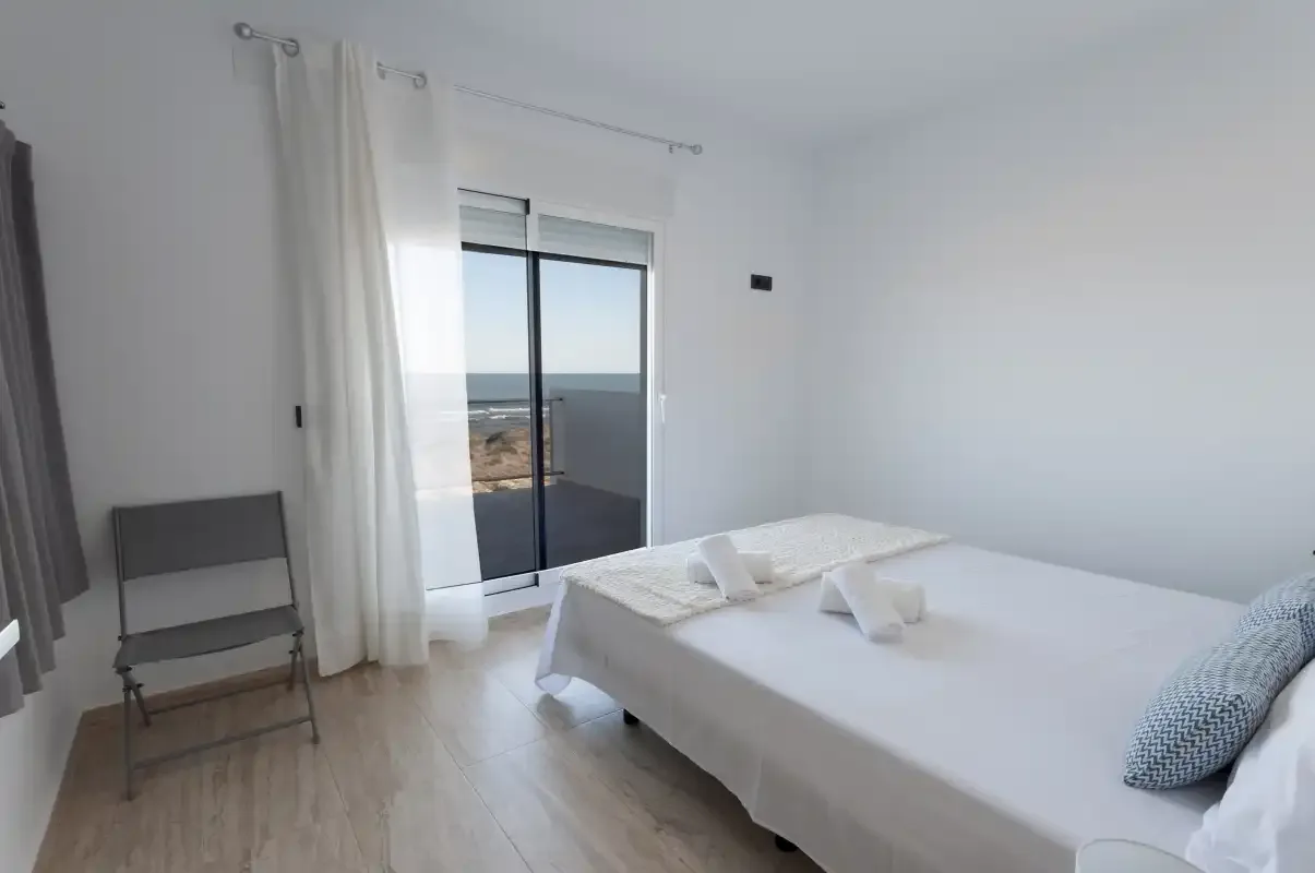 A bright bedroom with a white bed beside a large glass door.