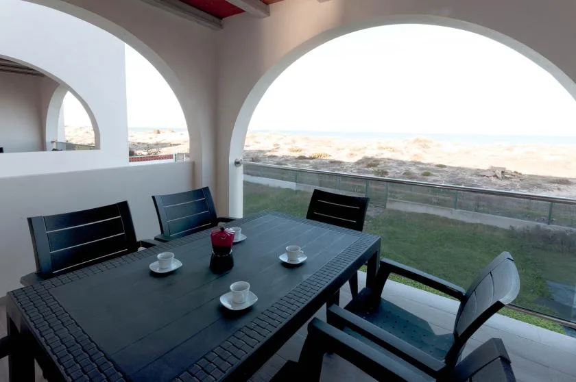 Un patio cubierto con una mesa oscura y sillas da a la costa.