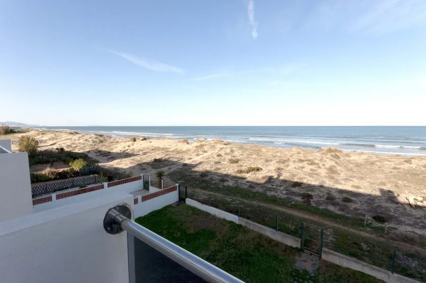 A coastal view shows sandy dunes and the ocean beyond a terrace railing.