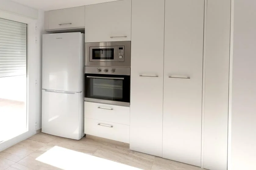 A bright kitchen with white cabinets, a refrigerator, and built-in cooking appliances.
