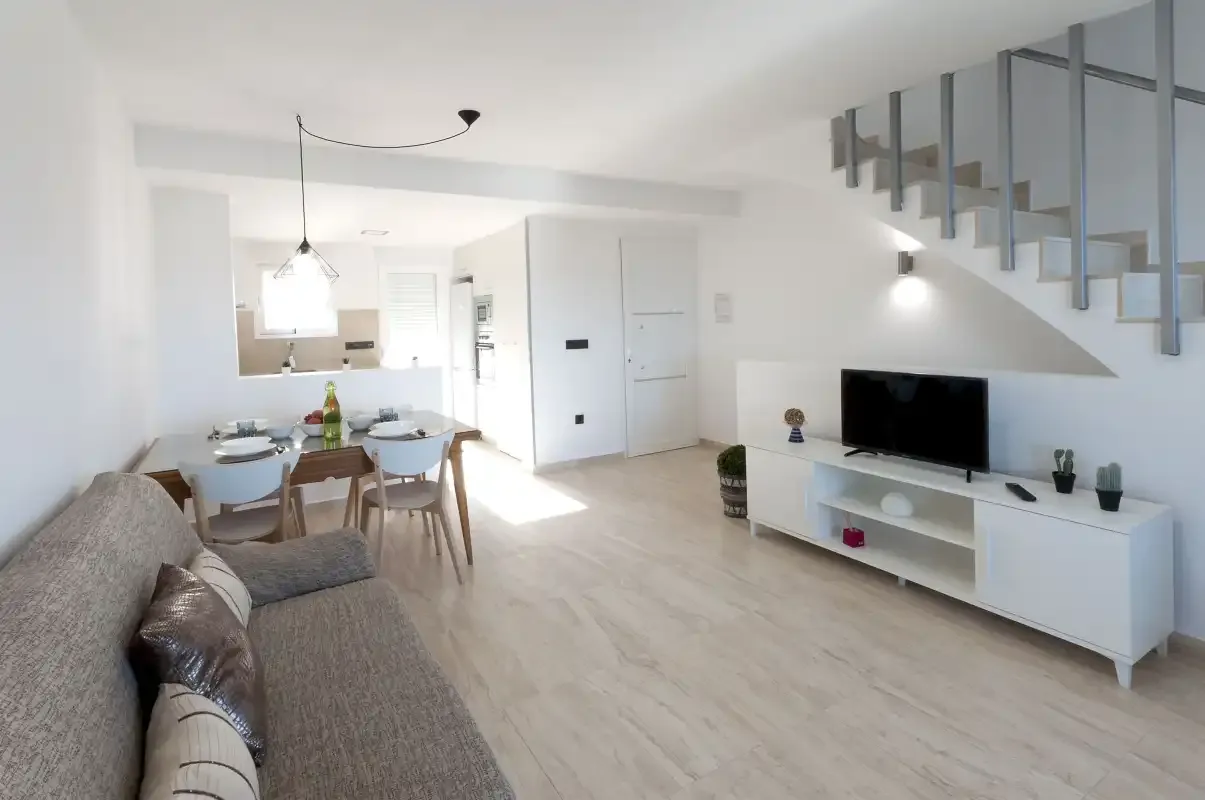 A bright living and dining area with seating, a television, and a staircase.