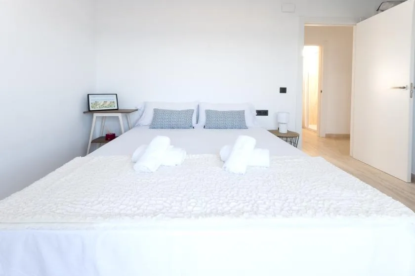 A bright bedroom with a neatly made bed and an open doorway.